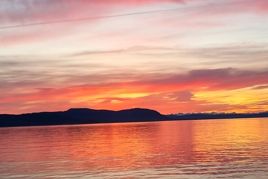 Sunset over calm water seen from a yacht, with a dark headland on the horizon