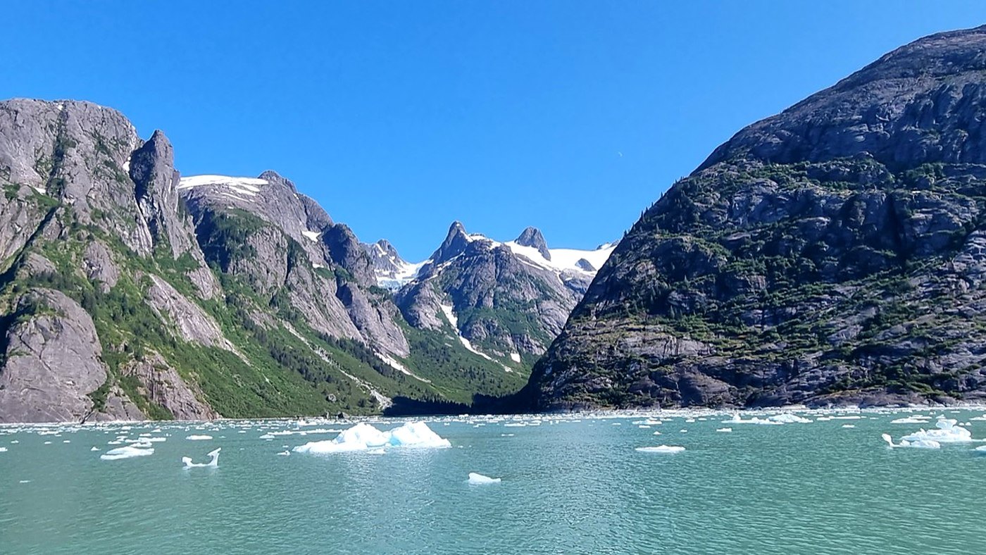Snow-capped mountains rising above an iceberg-dotted fjord on a clear day