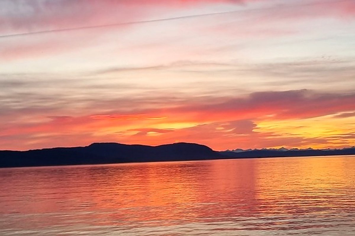 Orange and pink sunset sky over calm water and a dark headland